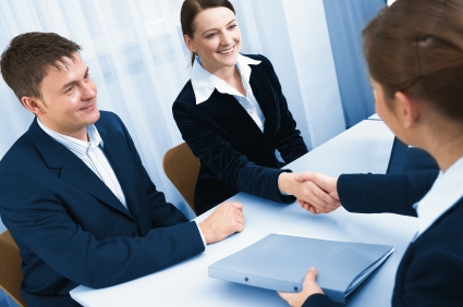 three or four people successfully smiling and shaking hands at a table